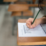 O ChatGPT disse: Pessoa preenchendo um cartão de respostas com lápis durante prova em sala de aula, em foco o movimento da mão e o formulário.