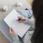 Uma jovem aluna parece concentrada e ansiosa enquanto escreve em um caderno, possivelmente estudando para a redação do ENEM